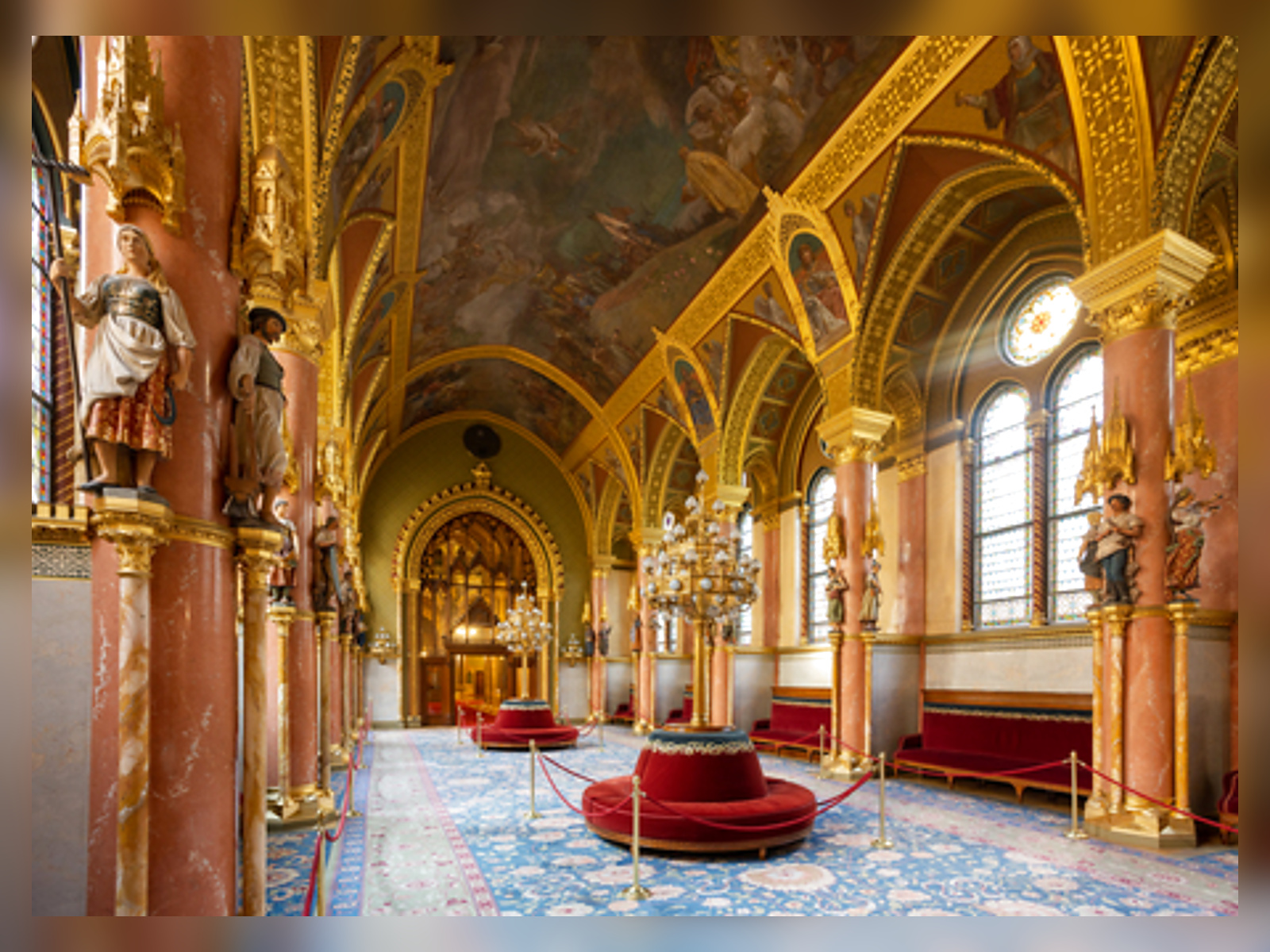A gilded lobby with red velvet benches and stained-glass windows